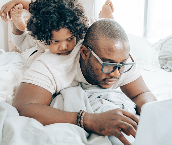 A small boy watching his dad working on a laptop from home